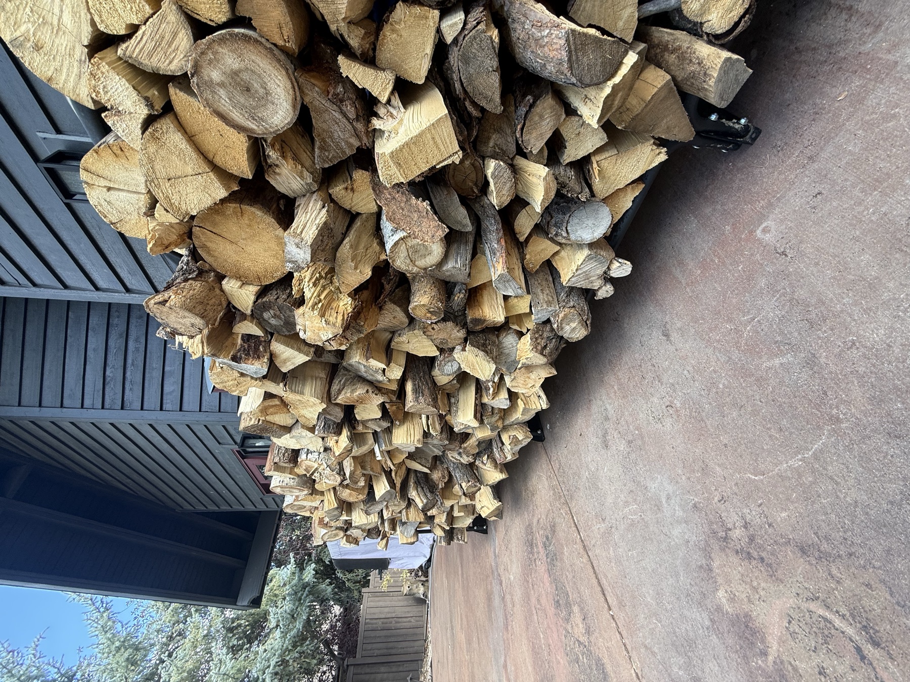 A full rack of split, seasoned firewood stacked along the side of a dark-stained Park City home