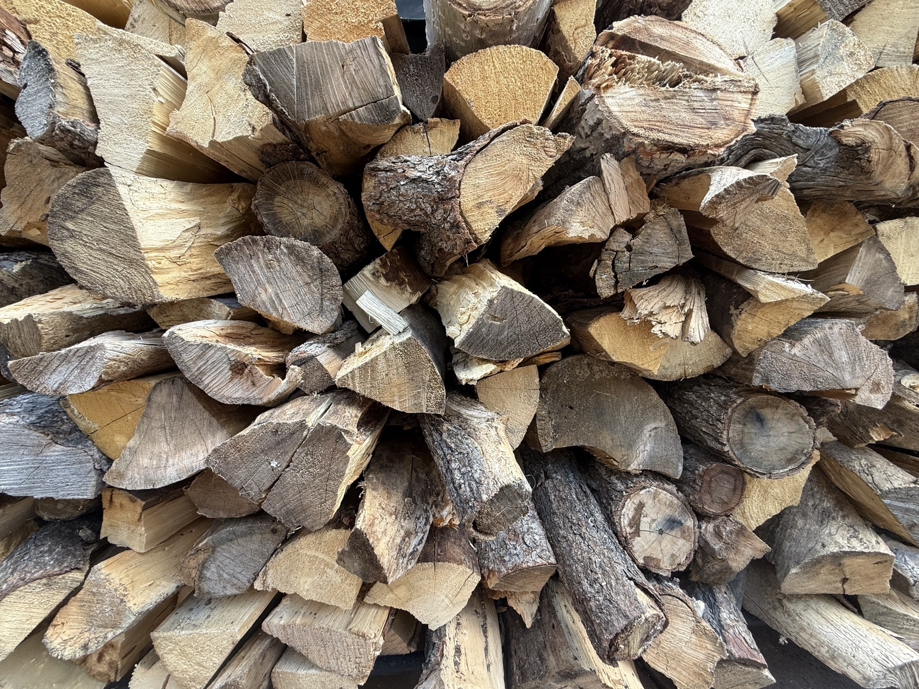 Split firewood stacked close, bark and end grain in warm light