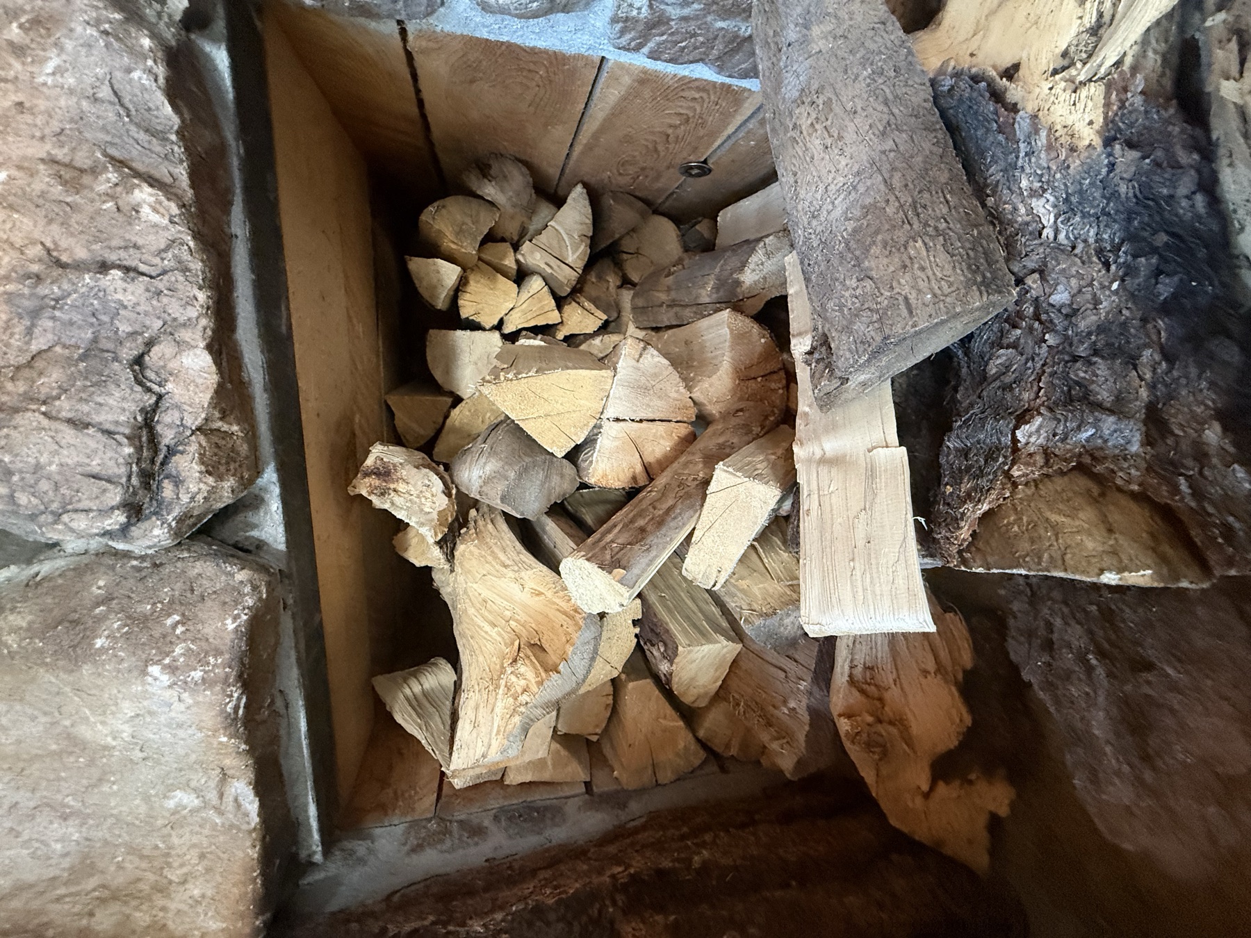 Split firewood stacked in a built-in wood niche set into a stone fireplace wall